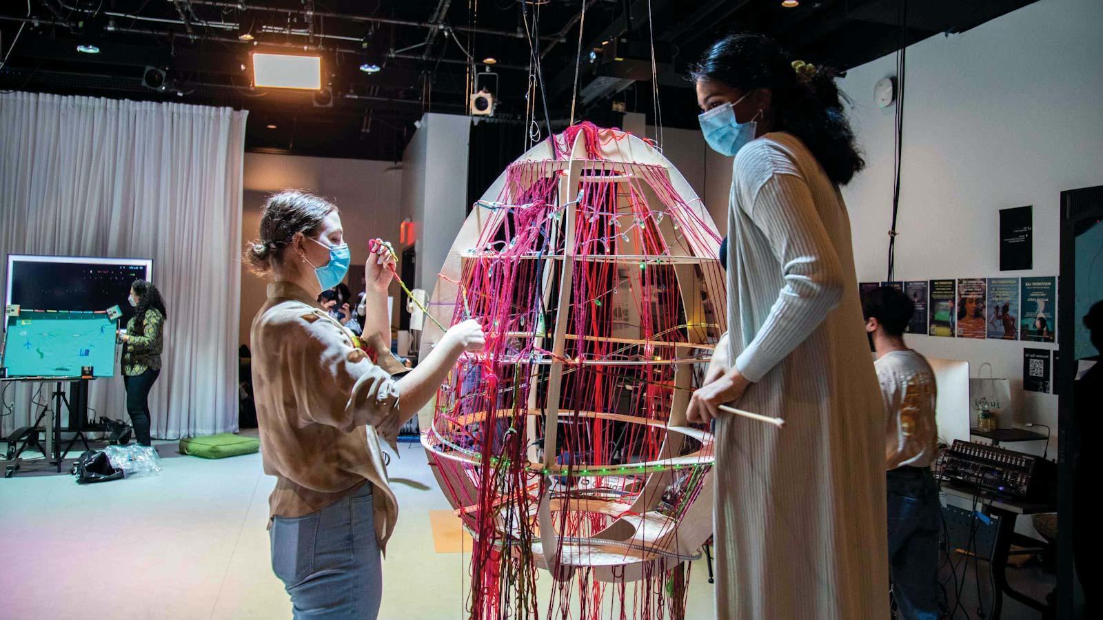 2名学生在一个巨大的蛋形物体上编织彩色纱线